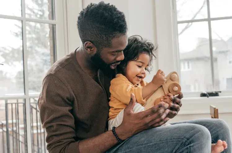 a toddler sits on his dad's knee